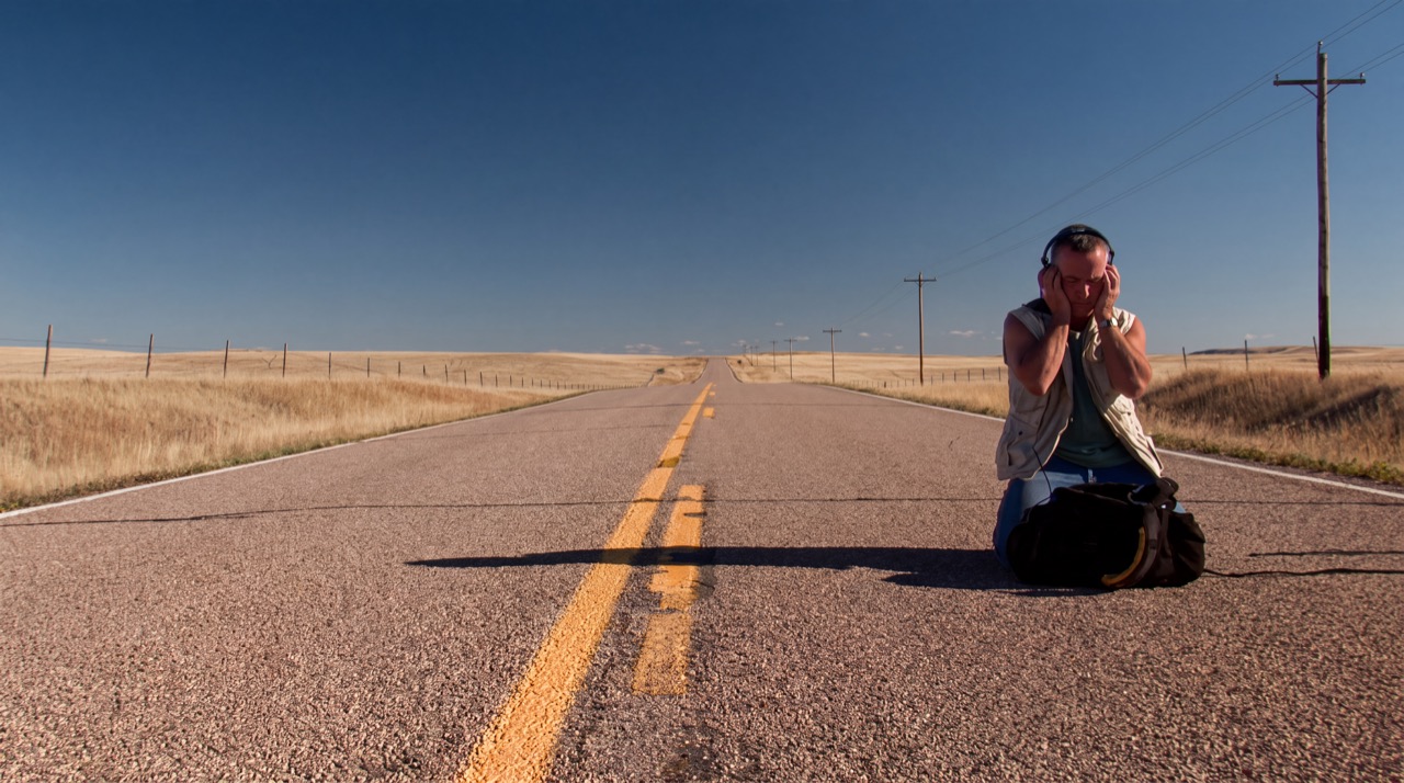 Gordon Hempton kneeling in headphones on an empty prairie highway, a still from Soundtracker